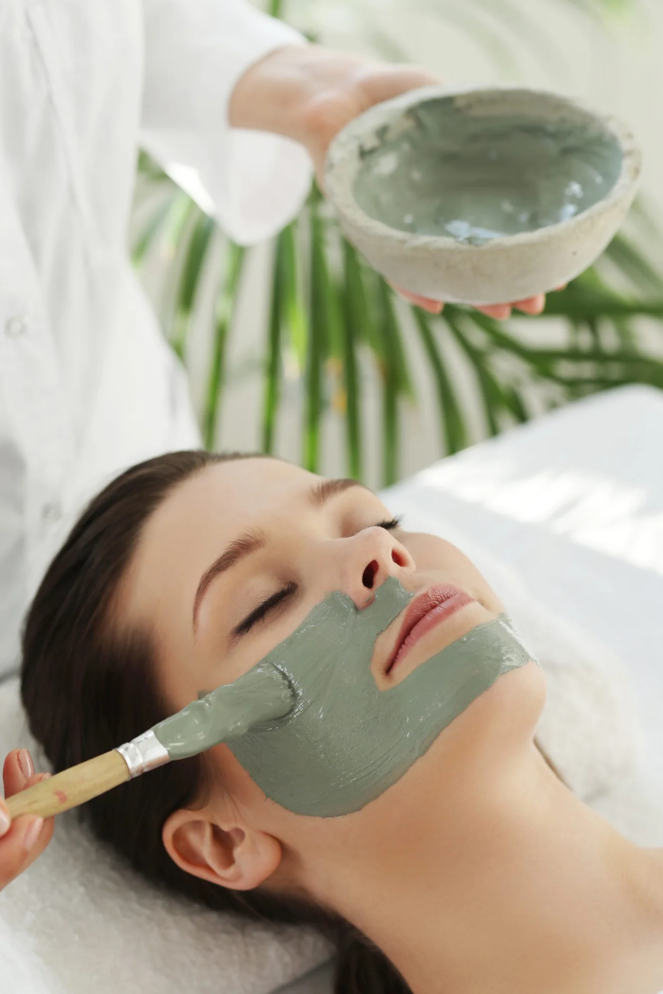 A clay treatment mask being brushed onto a client's face during a facial at Vitamin Medical Center